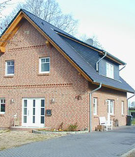 Ein Einfamilienhaus mit rotem Verblender und schwarzem Satteldach. Die Auffahrt ist anthrazit